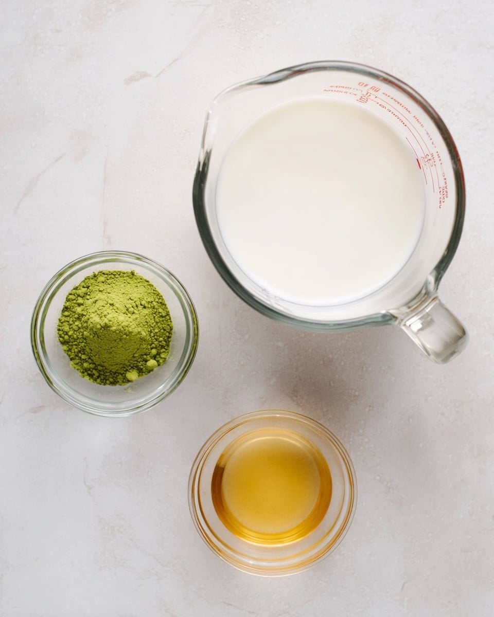 The image shows three clear glass bowls on a white marbled surface. The largest bowl on the right is a glass measuring cup filled with thick white liquid, likely milk. To the left and a little above, there is a small bowl with a vibrant green powder, possibly matcha. Below that green powder bowl, there is another small clear bowl containing a golden-yellow syrup or liquid. The bowls are spaced evenly and neatly arranged in a triangular form. Photo taken with an iphone --ar 4:5 --v 7