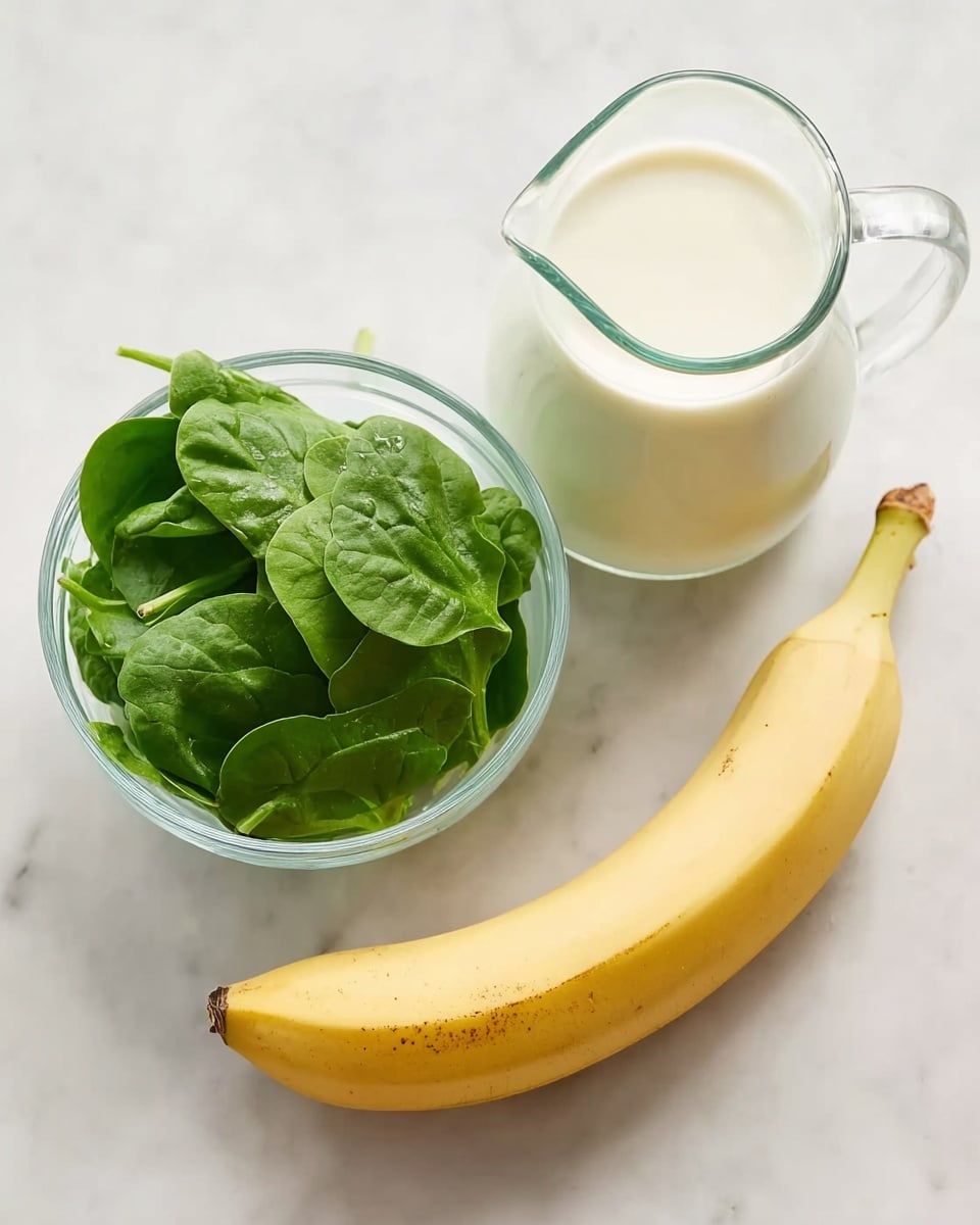 The image shows three separate clear glass containers placed on a white marbled surface. In the left container, there is a small pile of fresh green spinach leaves with smooth texture. On the top right, there is a clear glass pitcher filled with light creamy white milk, showing a smooth surface. Below the pitcher, a single ripe yellow banana with a few small spots is placed horizontally, with its curved tip pointing right. The overall view is clean and bright with soft natural light. Photo taken with an iphone --ar 4:5 --v 7