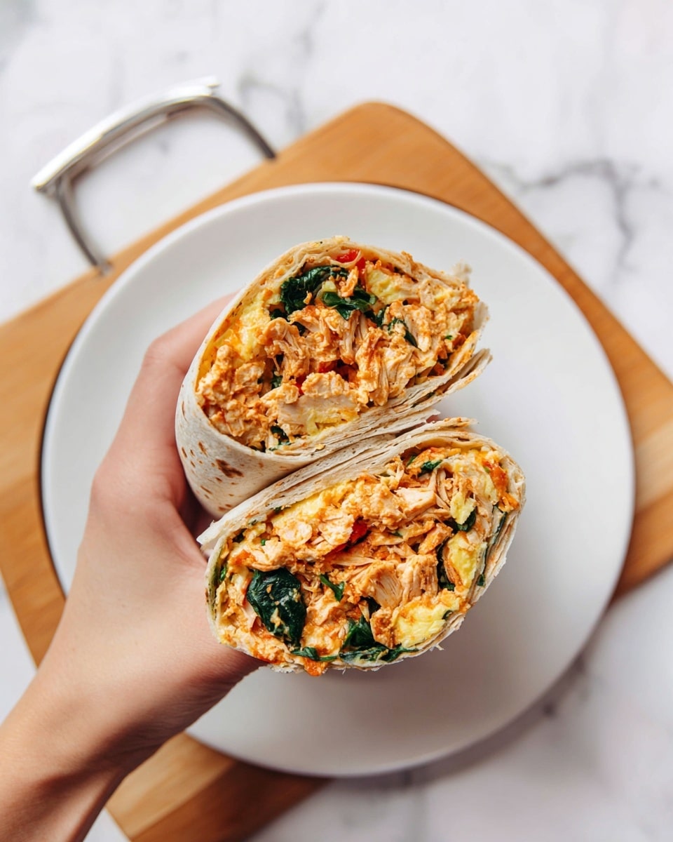 A woman's hand is holding a tortilla wrap cut in half to show four layers inside: the outer pale grayish-brown wrap with small dark spots, the first filling layer of shredded cooked chicken in an orange-red sauce, mixed with chopped dark green spinach leaves, followed by a soft, light yellow scrambled egg layer mixed with the chicken and spinach, all packed tightly inside the wrap halves. The wrap halves are held over an empty white plate, which sits on a wooden board with a metal handle, all placed on a white marbled surface. Photo taken with an iphone --ar 4:5 --v 7