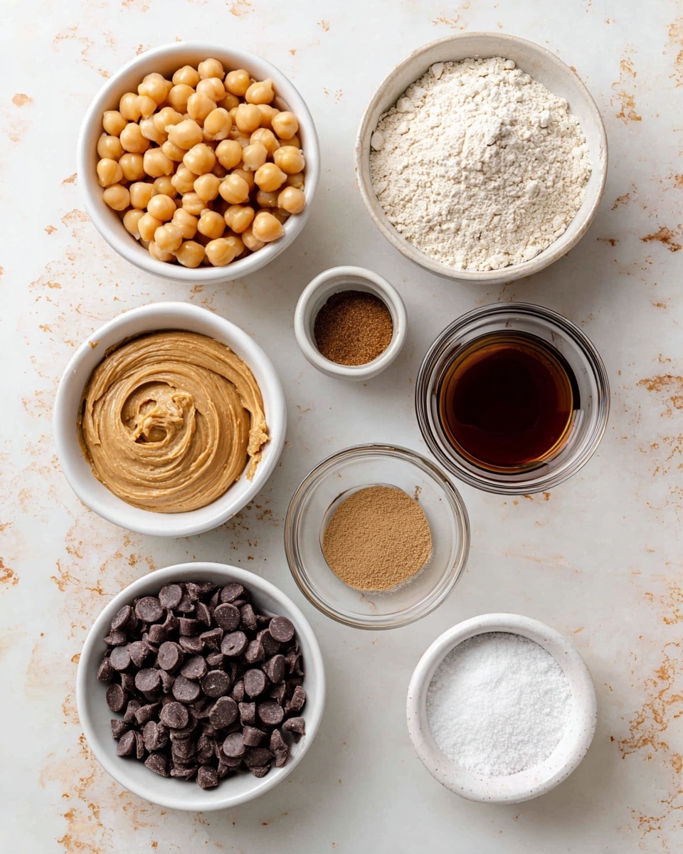 A white bowl filled with round, tan chickpeas sits at the top center. Below it to the left is another white bowl with smooth, light brown cashew butter displaying swirled texture. To the right of cashew butter is a small white bowl with a white powder of oat flour. Next to oat flour on the right is a clear glass bowl with dark brown maple syrup that looks thick and shiny. Below oat flour, a white bowl contains dark vegan chocolate chips, which are somewhat round and shiny. To the left of the chocolate chips, a small white bowl has light-colored salt and white baking soda powder mixed together. Below the salt bowl, another white bowl holds brown vanilla extract with a smooth surface. All bowls sit on a white marbled surface with light beige and brown scattered details. Photo taken with an iphone --ar 4:5 --v 7